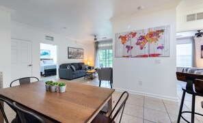 A modern living room with a dining area, a sofa, a coffee table, and a world map artwork on the wall.
