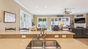 A modern kitchen with a central island, a dining area with chairs, a sofa, and a TV in the living room.