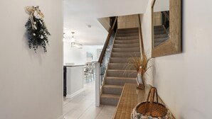 Una escalera con alfombra estampada, una cesta de mimbre con conchas marinas y un espejo en la pared.