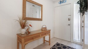Un pasillo limpio y minimalista con una consola de mimbre, un espejo y una puerta con la leyenda 'Beach'.