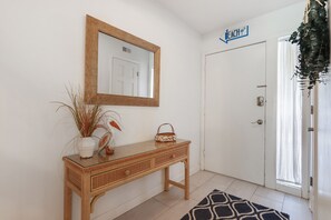 Un couloir épuré et minimaliste, avec une console en osier, un miroir et une porte portant l’inscription « Plage ».