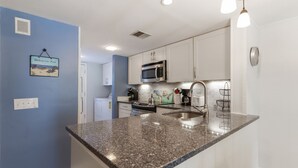 Una cocina con gabinetes blancos, encimera de granito, microondas de acero inoxidable y un lavamanos.