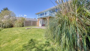 A house with a blue balcony, a grassy yard, and tall grass in front.