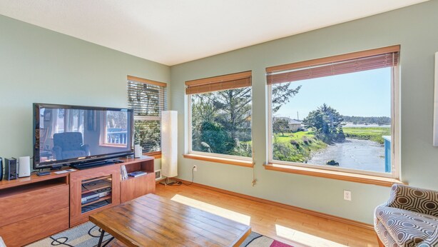 A living room with a TV, wooden furniture, large windows, and a view of a landscape.