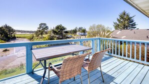 A deck with a table and chairs, overlooking a body of water and distant buildings.