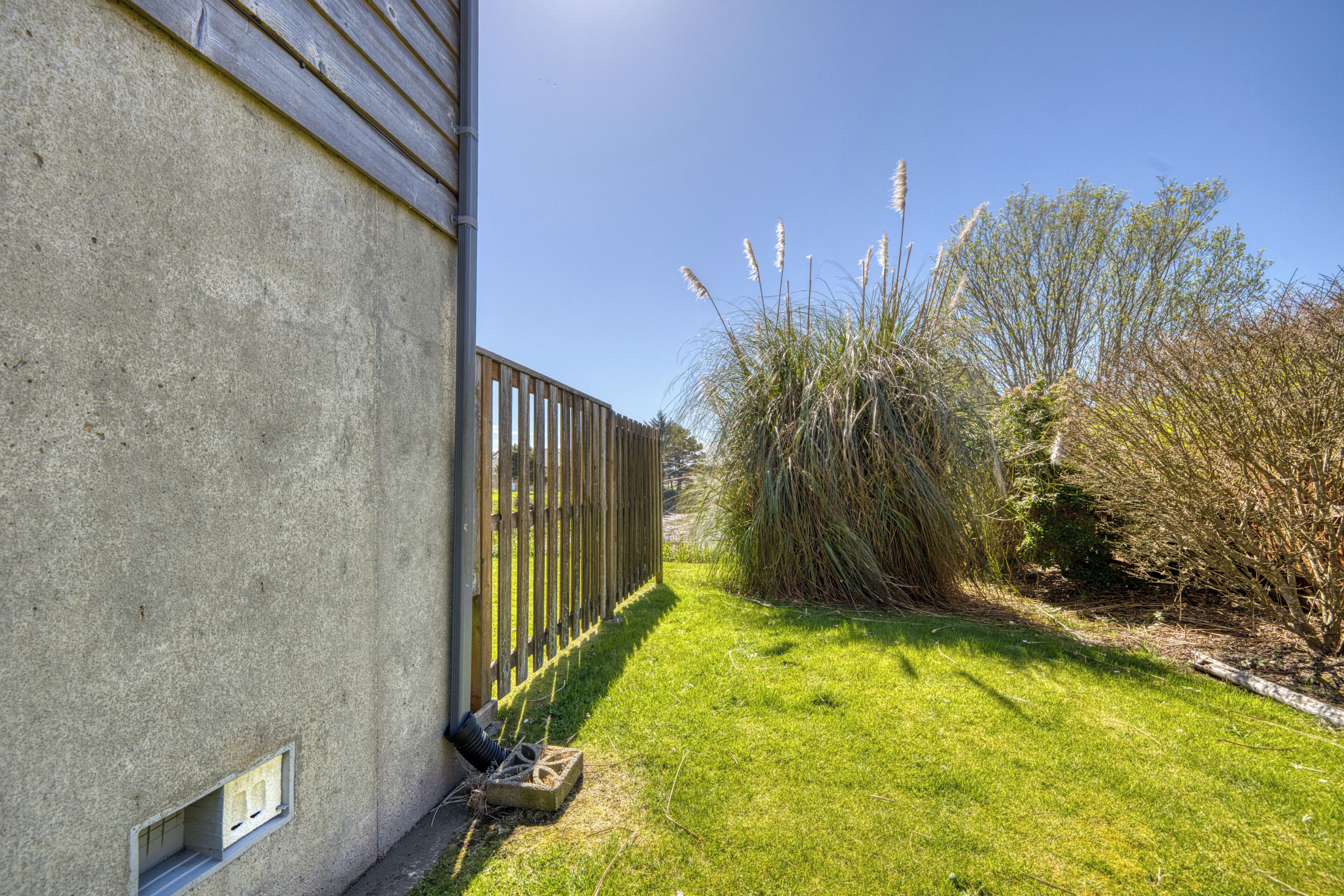 A concrete building with a wooden fence, a grassy yard, and tall grasses.