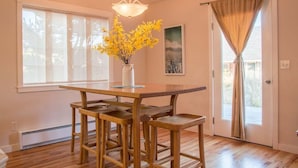 A dining area with a wooden table and bar stools, a vase with yellow flowers, and a cityscape painting on the wall.