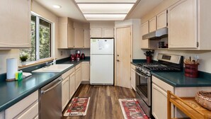 A compact kitchen with light wooden cabinets, a white refrigerator, a stove, and a sink. - Mountain Crest Getaway: Mountain & Slope Views! Pool Table! Gas Fireplace! Cable! Pet Friendly! WiFi! (Big Bear City)