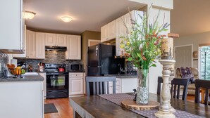 A modern kitchen with white cabinets, a black refrigerator, and a wooden dining table with a vase of flowers.