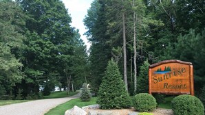 A wooden sign for Sunrise Resort surrounded by a gravel path, trees, and well-maintained landscaping. - Lakefront Cabin #4 The Crappie (Presque Isle)