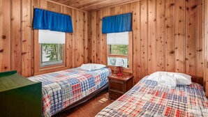 Une chambre de style cabane avec deux lits, des murs en bois et de grandes fenêtres ornées de rideaux bleus.
