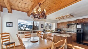 Una cocina con armarios de madera, un refrigerador negro y un comedor con mesa y sillas de madera.