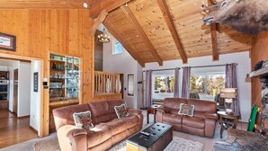 Ein gemütliches Wohnzimmer mit Holzbalkendecke, Kamin und montiertem Tierkopf.