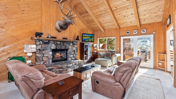 Ein gemütliches Blockhaus-Interieur mit Kamin aus Stein, Ledersofas und einem aufgehängten Hirschkopf.