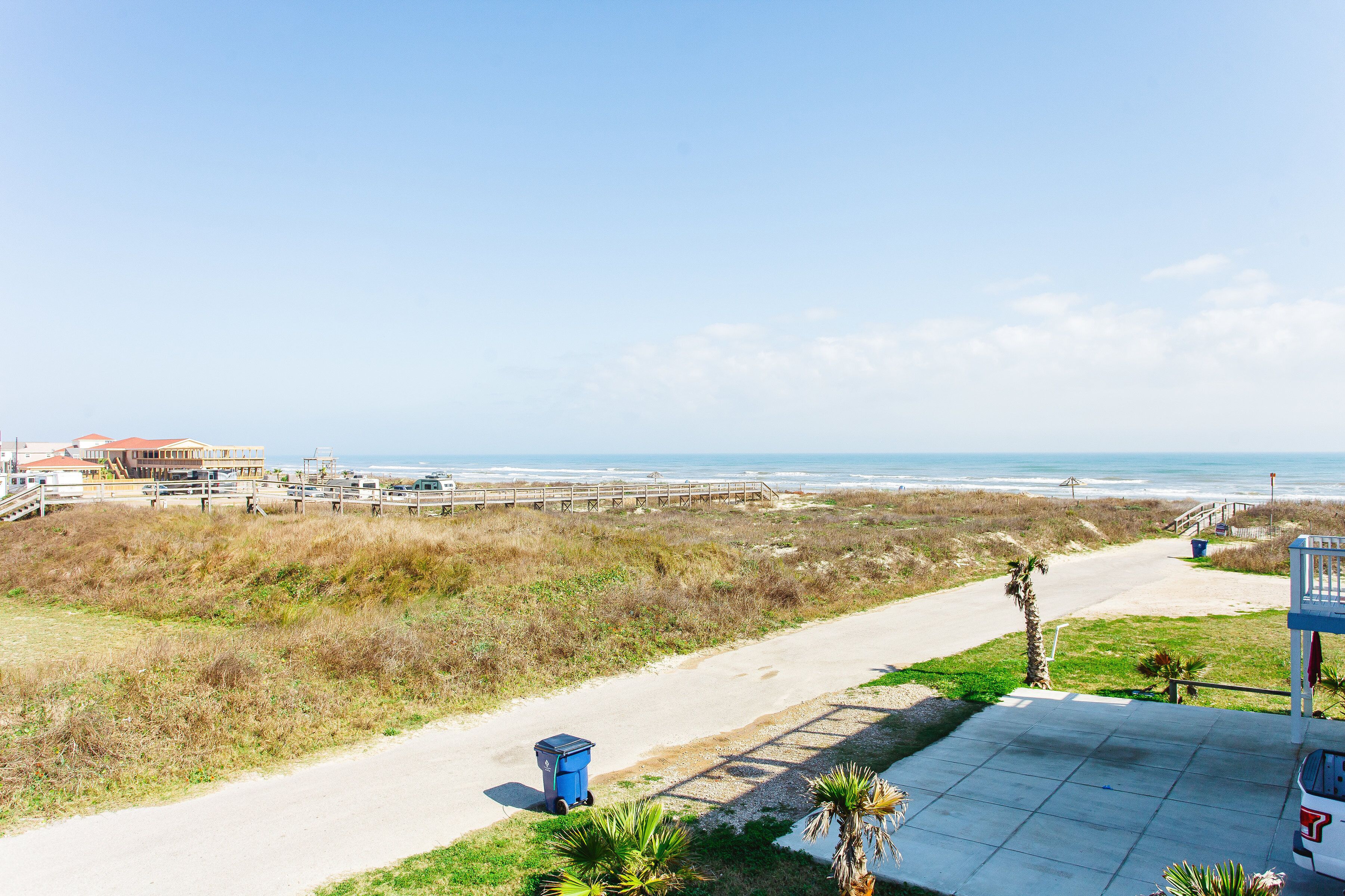 A coastal road with a beach view, a blue trash bin, and a lifeguard tower.