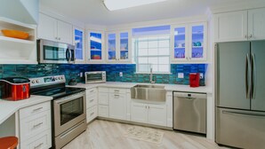 Een moderne keuken met witte kasten, roestvrijstalen apparatuur, een blauwe achterwand en een raam met uitzicht.