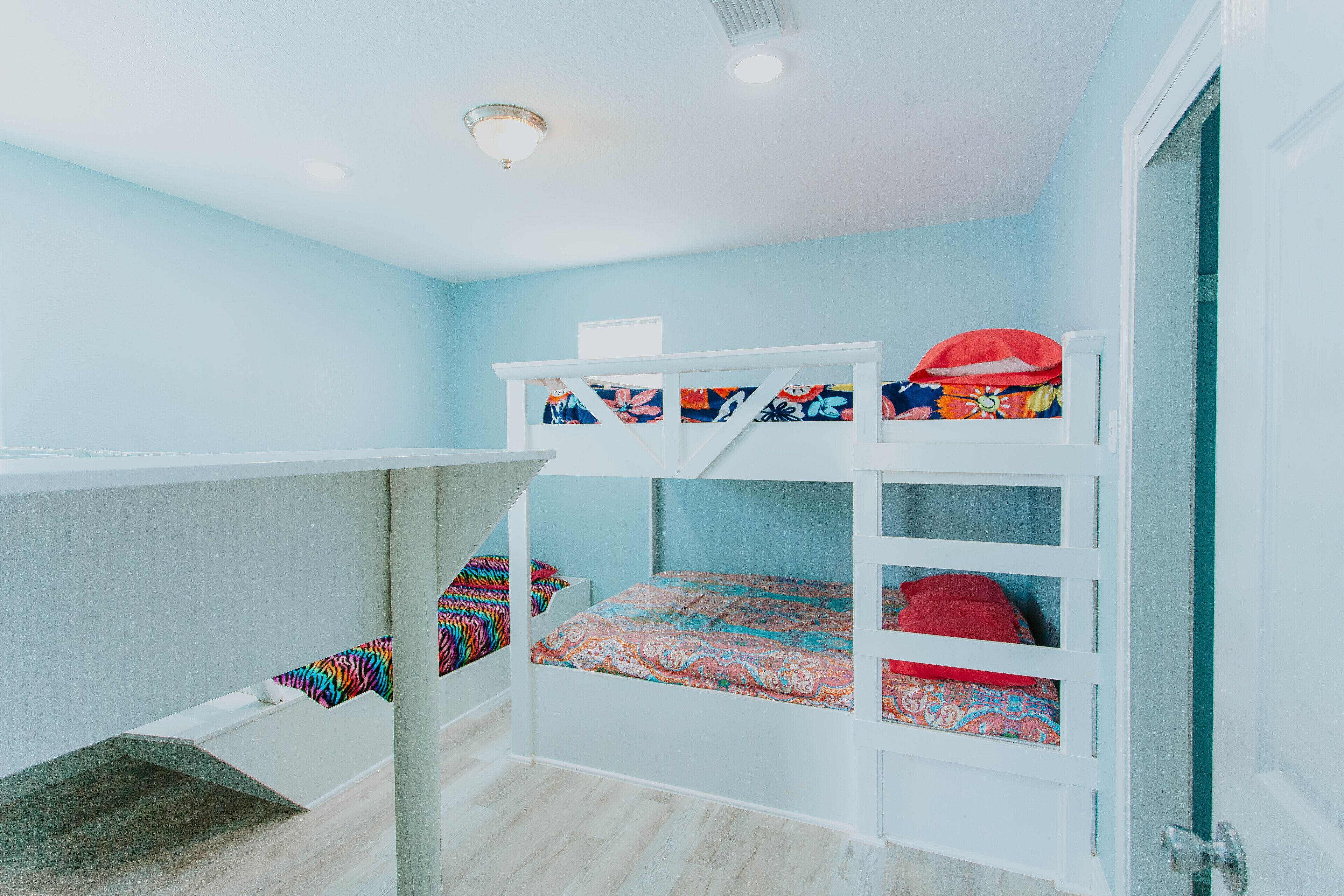 Habitación con literas de estructura blanca, colcha colorida y almohada roja.