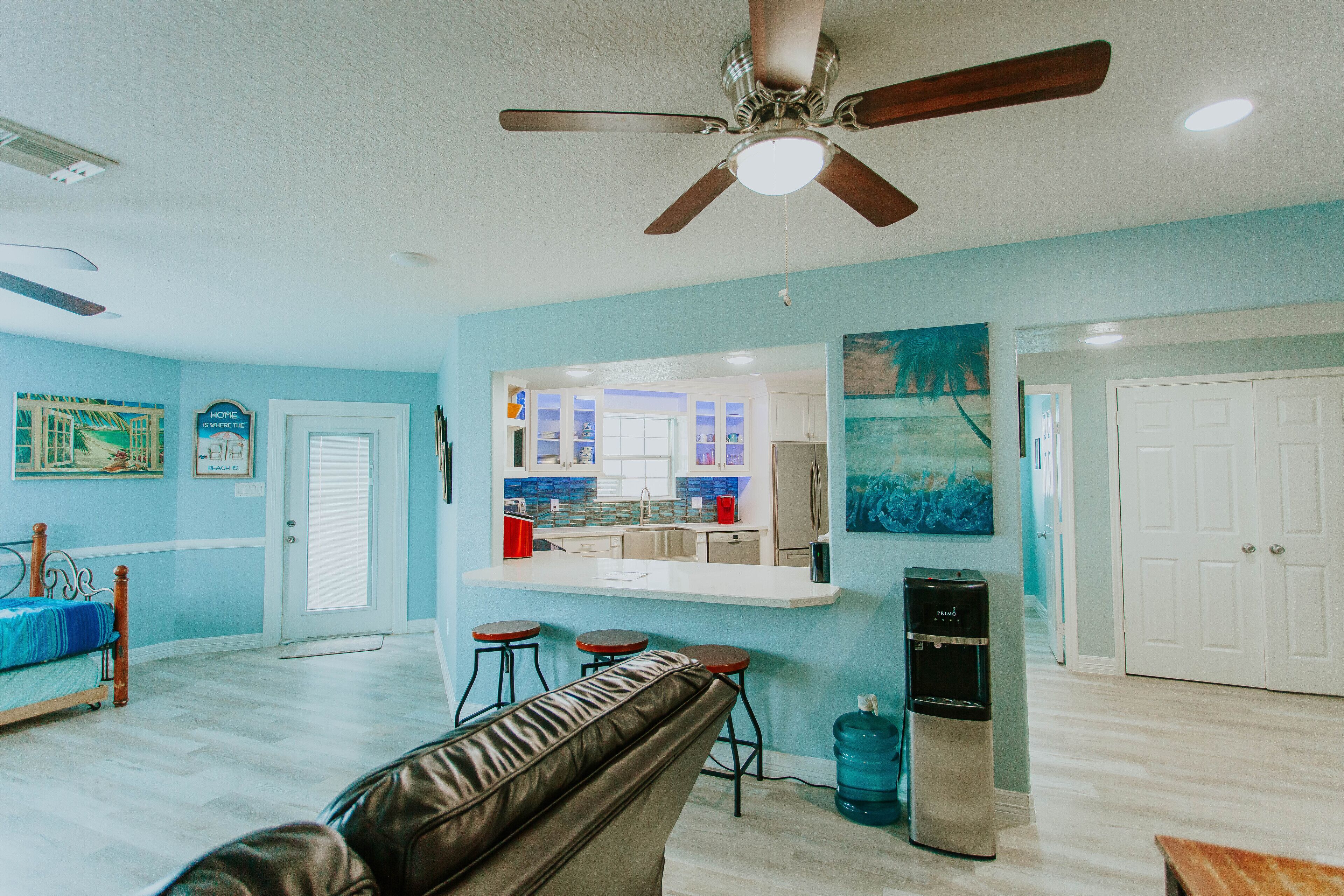 A room with a ceiling fan, a kitchenette, a water dispenser, and a bench.