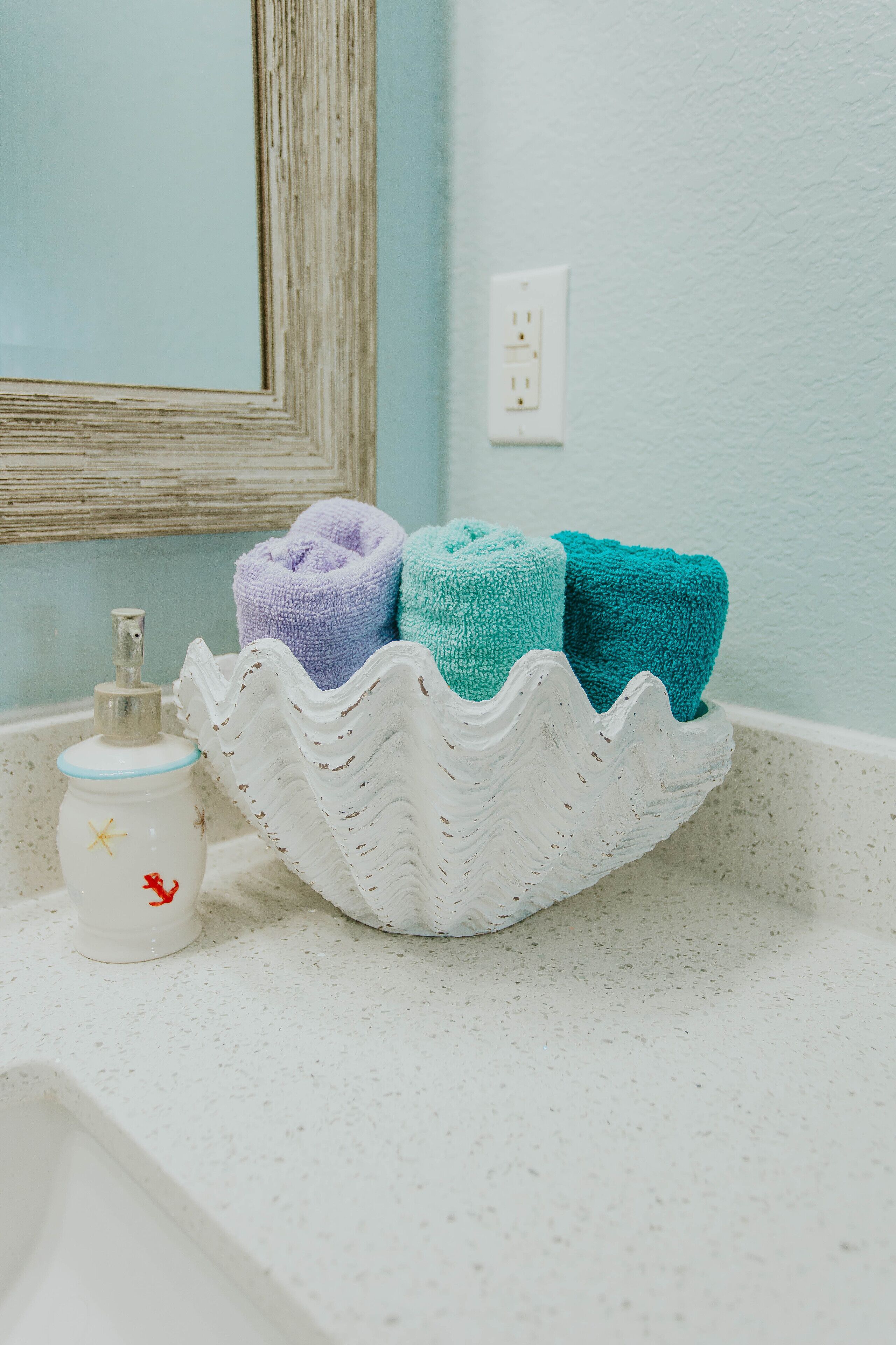 A bathroom sink with a decorative soap dispenser and a soap dish, a white soap dish with a wavy edge, and a white basin with towels.