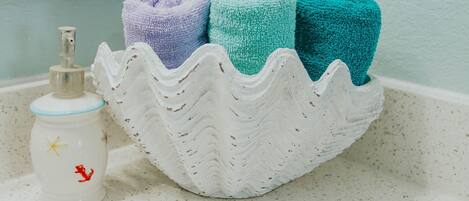 A bathroom sink with a decorative soap dispenser and a soap dish, a white soap dish with a wavy edge, and a white basin with towels.
