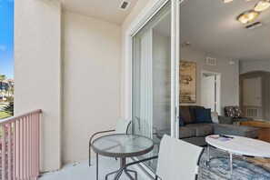 A balcony with a glass door, a round table, and a sofa inside a room. - Resort Condo 3BR w Lake Access near Disney Orlando (Orlando)