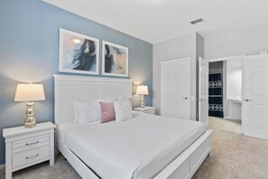 A bedroom with a white bed, two bedside lamps, a nightstand, and a door leading to a bathroom. - Resort Condo 3BR w Lake Access near Disney Orlando (Orlando)