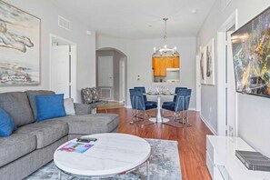 A modern living room with a grey sofa, a round coffee table, and a dining area with blue chairs and a white table.