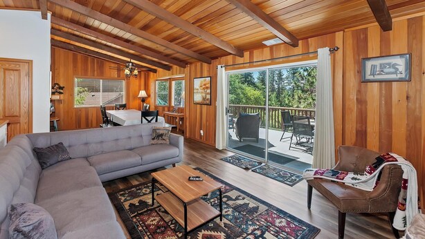 Un intérieur de chalet chaleureux avec un plafond en bois, un coin repas, un canapé, une table basse et une vue sur l’extérieur grâce à une porte-fenêtre coulissante.