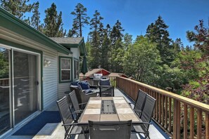 Una veranda coperta con tavolo e sedie, un barbecue e vista su una zona boschiva.