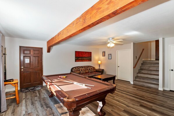 A room with a pool table, a sofa, a lamp, and a staircase.