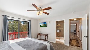 Une chambre avec un grand lit, un ventilateur de plafond, une télévision et un balcon doté d’une balustrade rouge.