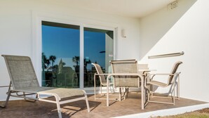 Un patio con cuatro sillas de mimbre y una mesa, una puerta de cristal que da al exterior, y una pared blanca con un letrero de advertencia.