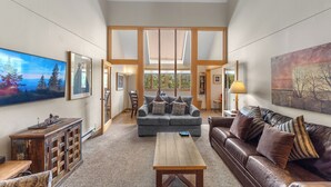Un salon spacieux avec un plafond haut, un canapé gris, une table basse en bois et un divan en cuir marron.