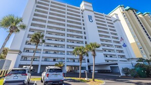A multi-story hotel with a prominent '6' on the facade, palm trees in front, and a parking area with cars. - "Breakers East 205"~Spacious 2BR/2BA Gulf Front Condo Beach setup included (Destin)