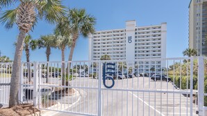 A gated parking area with a building in the background, palm trees, and a clear sky. - "Breakers East 205"~Spacious 2BR/2BA Gulf Front Condo Beach setup included (Destin)