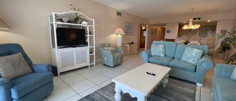 Una sala de estar con un televisor sobre un mueble blanco, un sofá azul, un sillón a juego y una mesa de centro.