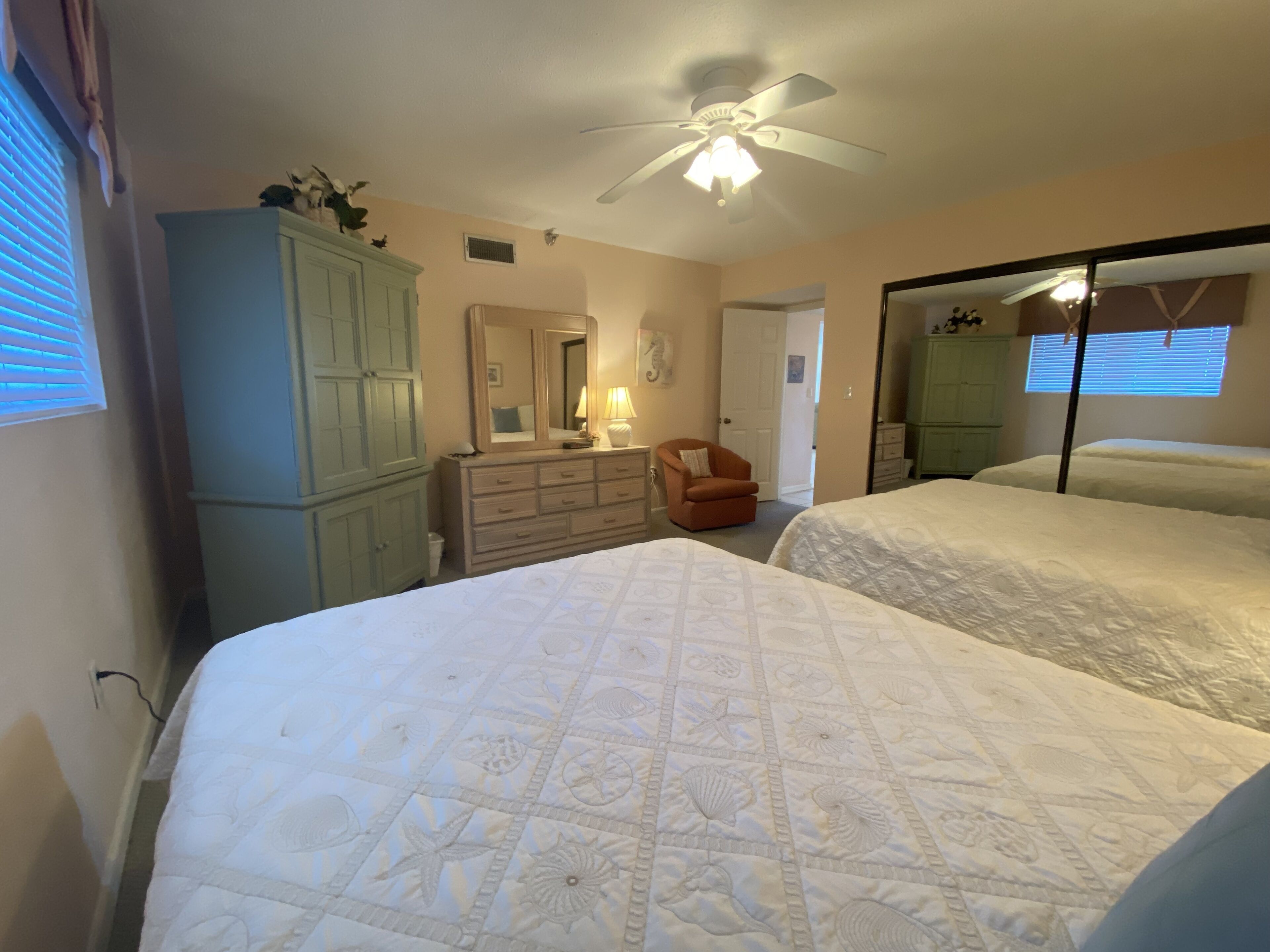A bedroom with two beds, a ceiling fan, a dresser, and a mirror.
