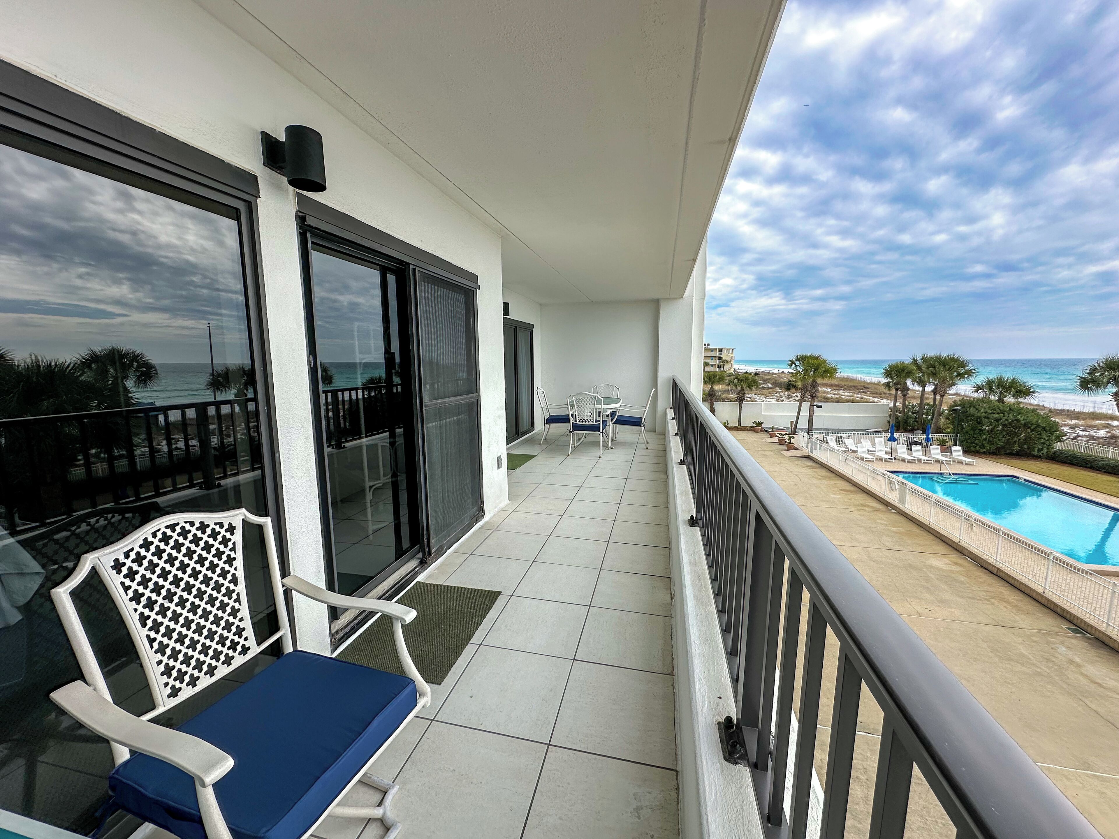 A balcony with a view of the ocean, a pool, and outdoor seating.