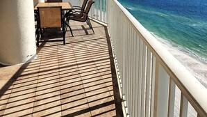 Un balcón con suelo de madera, una mesa y dos sillas, con vista a un mar azul y despejado.