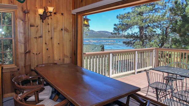 A wooden deck with a table and chairs, overlooking a body of water and trees. - Lake Views! Lakefront! BBQ! Internet! Close to the Village! (Big Bear Lake)
