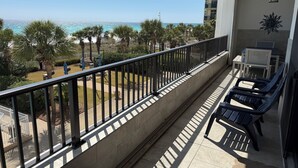 A balcony with a view of the ocean, a seating area with chairs, and a table.