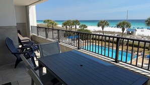 A balcony with a pool, chairs, and a view of the beach.