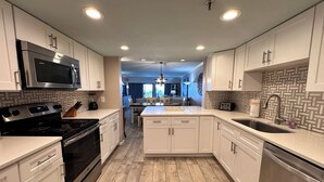 A modern kitchen with white cabinetry, stainless steel appliances, and a wooden floor.