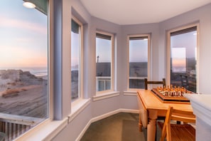 Enjoy the ocean view from this corner room, featuring a wooden table with a chessboard and three windows with a view of the beach.