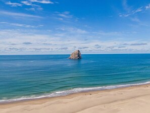 Une plage avec une grande formation rocheuse dans l’eau et un rivage sablonneux.