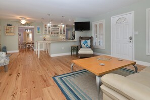 Un salón amplio con pisos de madera, una zona de comedor y una cocina al fondo, además de un televisor montado en la pared.