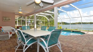 A covered patio with a pool, white table and chairs, and a ceiling fan. - Key West Style Waterfront, Private Pool, WiFi, Close to Village & Beaches Pet OK (Safety Harbor)