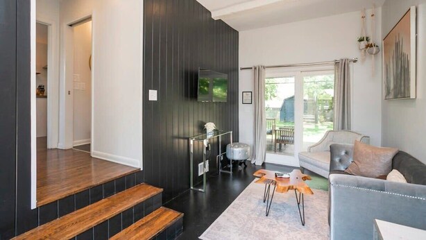 Ein modernes Wohnzimmer mit grauem Sofa, einer Holztreppe und einem flachbildfernseher an der Wand.