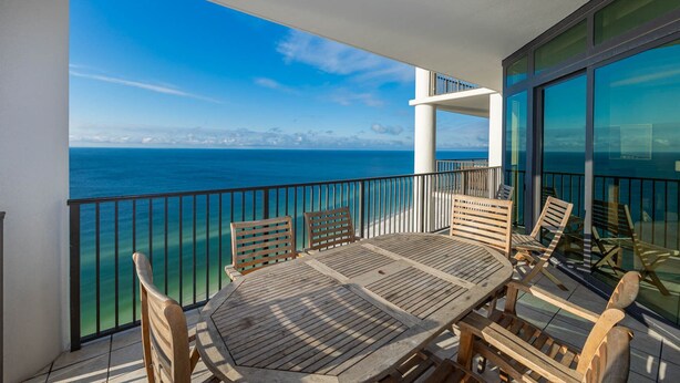 Ein Balkon mit Holztisch und -stühlen mit Blick auf das klare, blaue Meer.