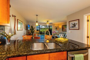 A kitchen with granite countertops, stainless steel sinks, wooden cabinets, and a dining area with a table and chairs.